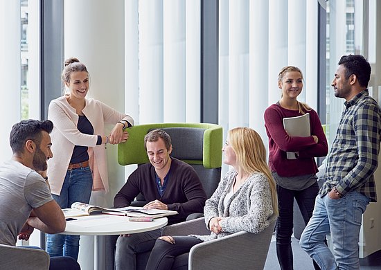 Sechs junge Menschen stehen und sitzen im Lesesaal